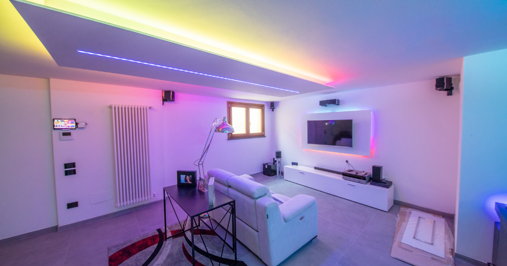 Colorful light along the ceiling of a small bedroom.